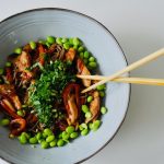 Top view of a vibrant Asian salad with edamame and noodles in a ceramic bowl.