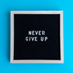 Black letter board with 'Never Give Up' message on a vibrant blue background.